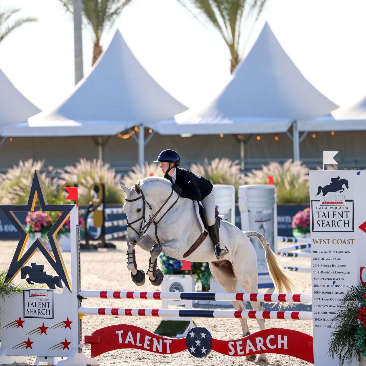 A rider on a gray horse jumping over the Talent Search fence.
